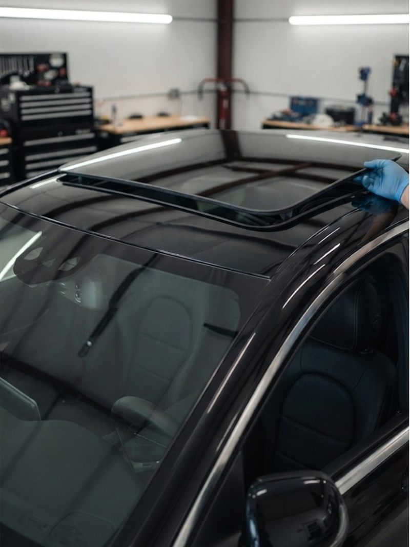 Technician fitting a sunroof glass panel on a black car in workshop